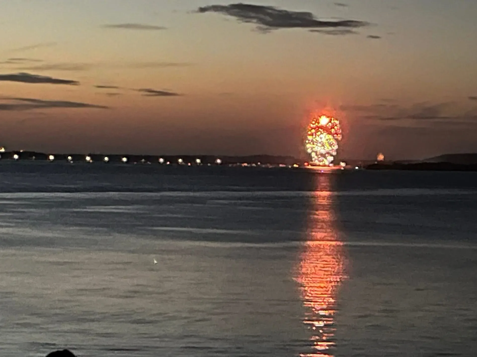 Orange firework display reflected on calm Lake Hudson water at dusk