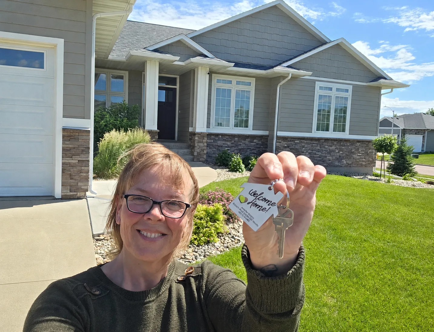 Jennifer Krosch holding a house-shaped keychain in front of a suburban Sioux Falls home