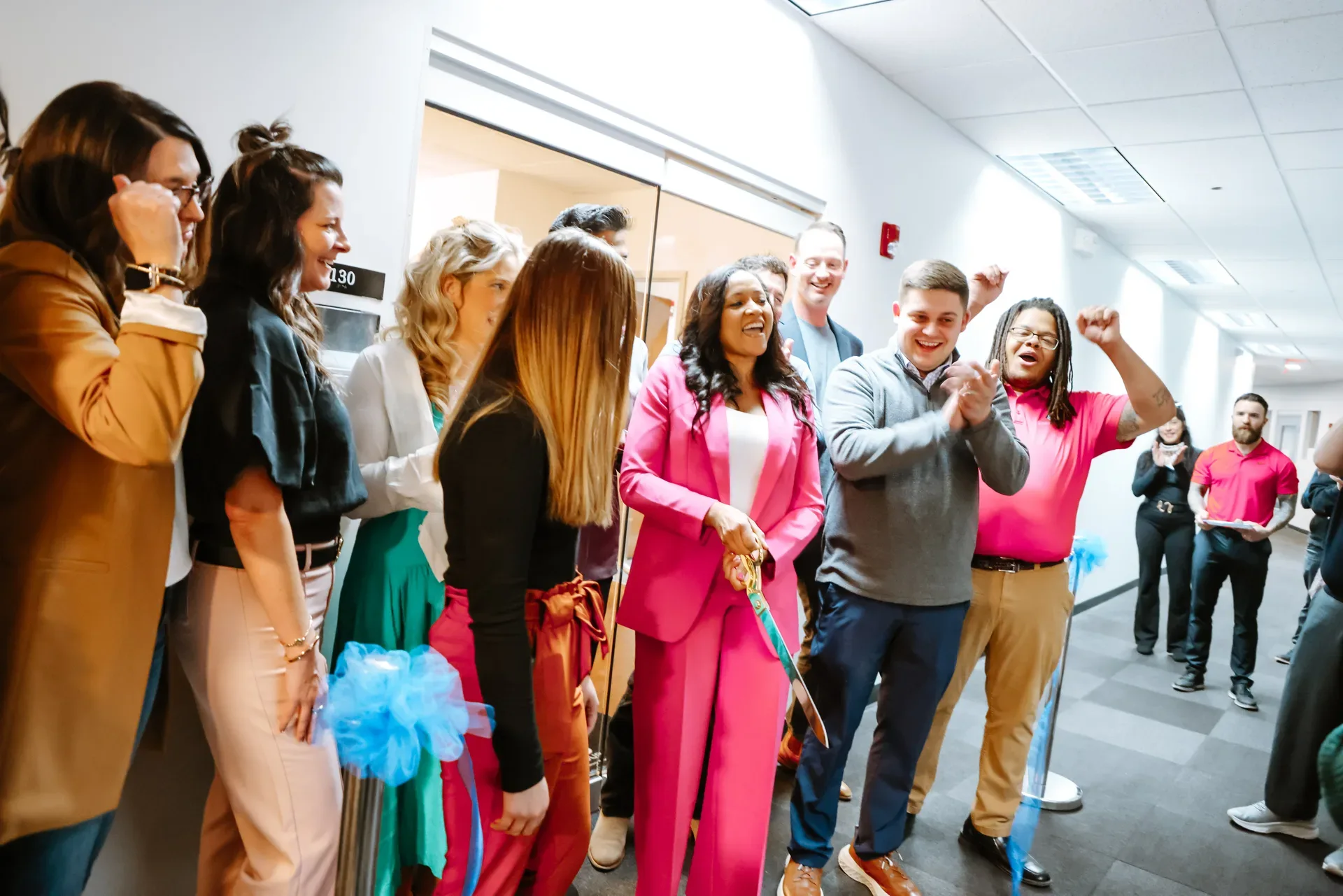 Korrin Ziswiler in a bright pink suit cutting the blue ribbon at the Glasshouse Realty Springfield office opening, surrounded by staff