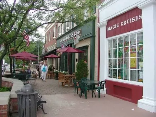 Brick storefronts and a Coffee & Tea House cafe with red umbrellas along downtown Worthington Ohio, with an American flag and pedestrians on the sidewalk