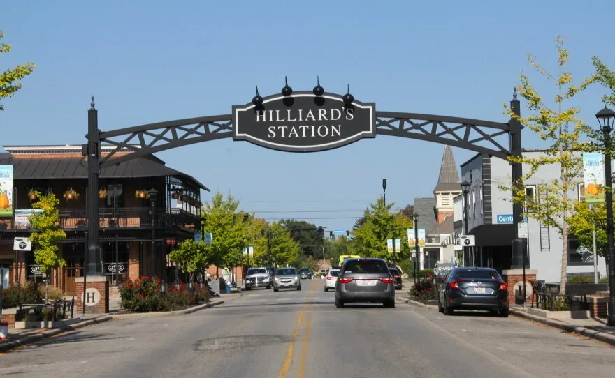 The black metal Hilliard Station archway spanning the downtown Hilliard Ohio street, with brick commercial buildings lining the sidewalks