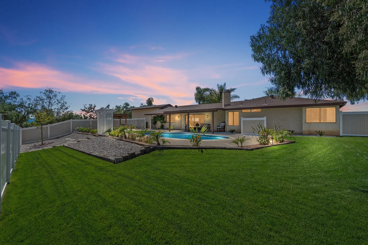 Exterior twilight shot of the house backyard with swimming pool and landscaped lawn