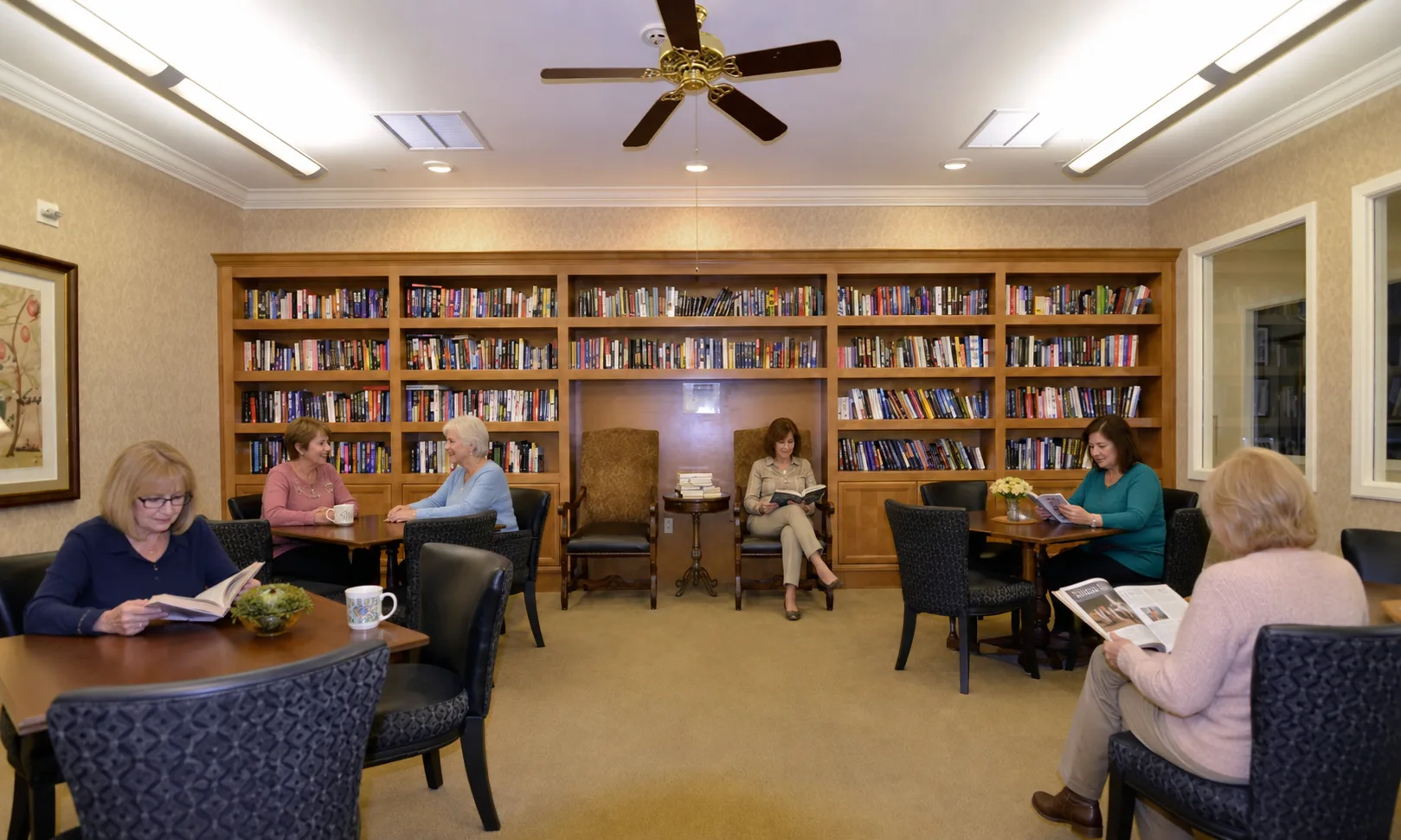 Several women seated in a quiet community library room with tall wooden bookshelves at The Colony