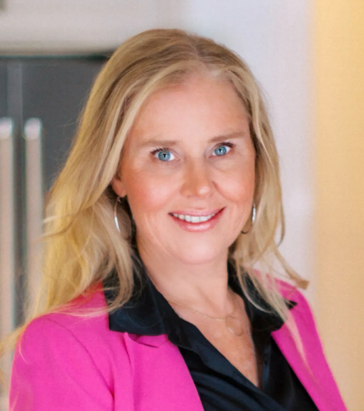 Tracie Carter, REALTOR® in a pink blazer, smiling in front of a bright backdrop