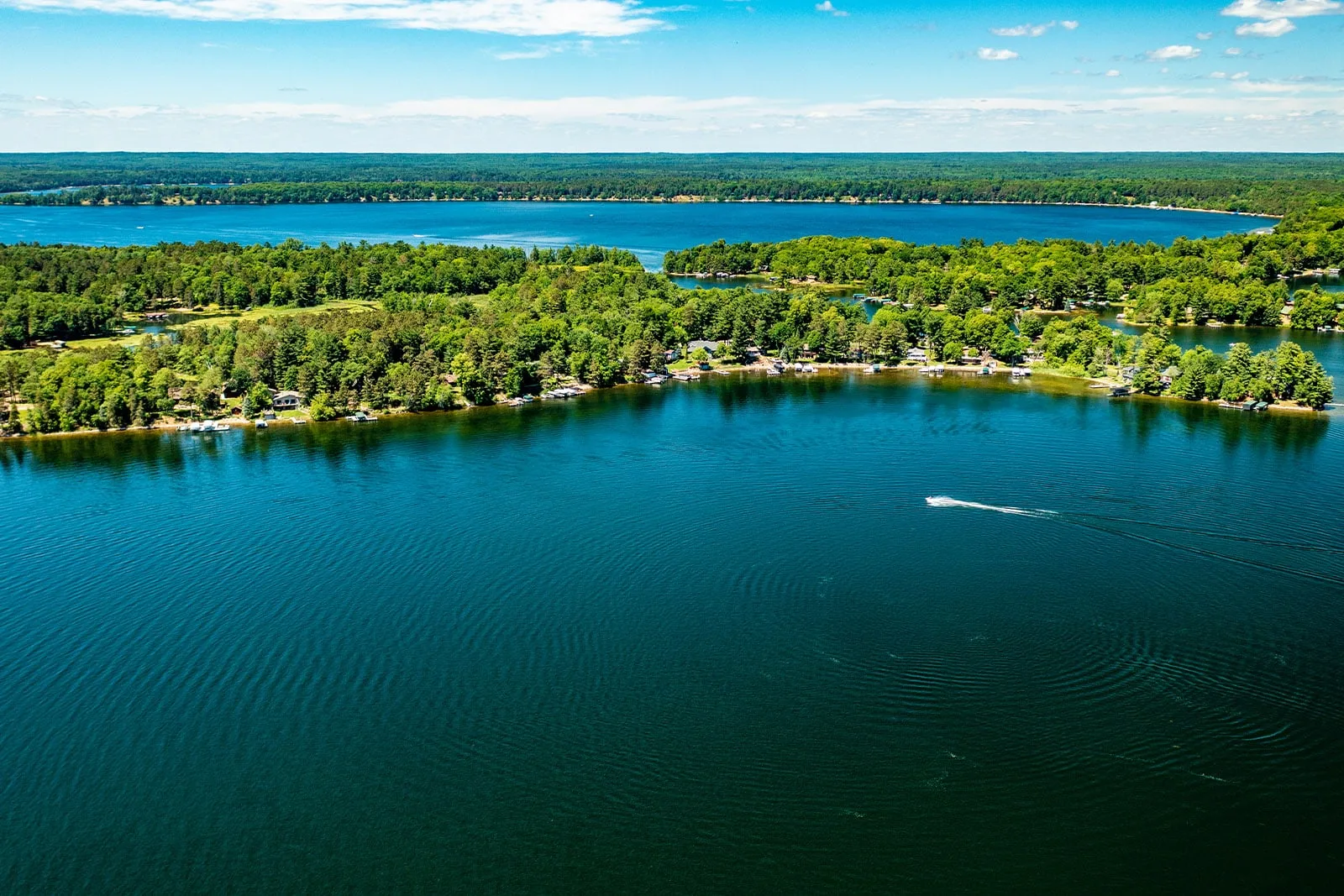Aerial drone shot of a scenic lake surrounded by dense green forests with a small boat on the water