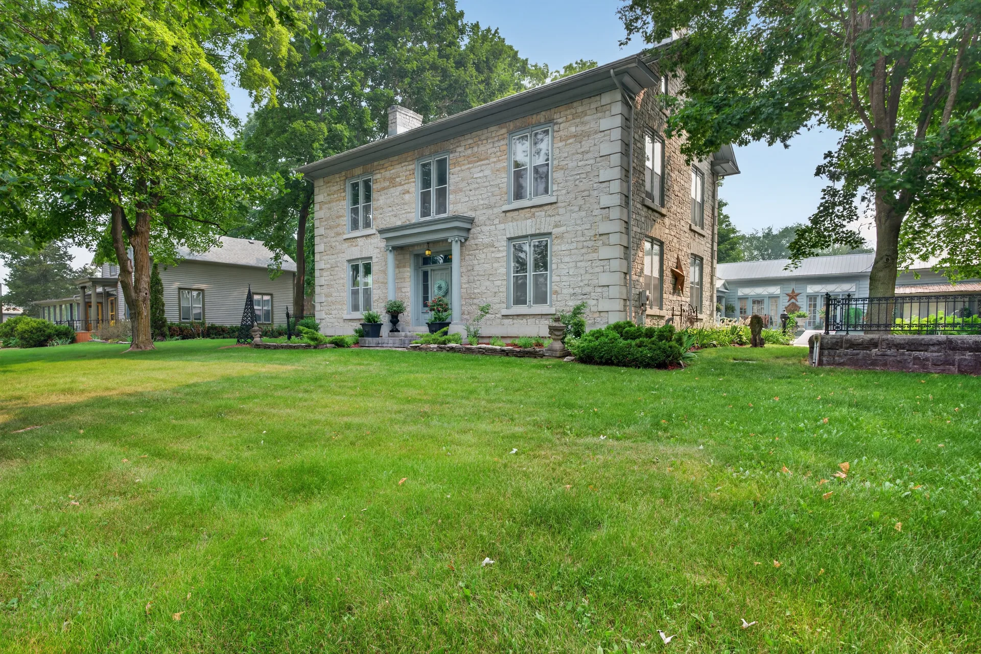 Historic two-story stone house with a lush green lawn surrounded by mature trees in Kingston Ontario