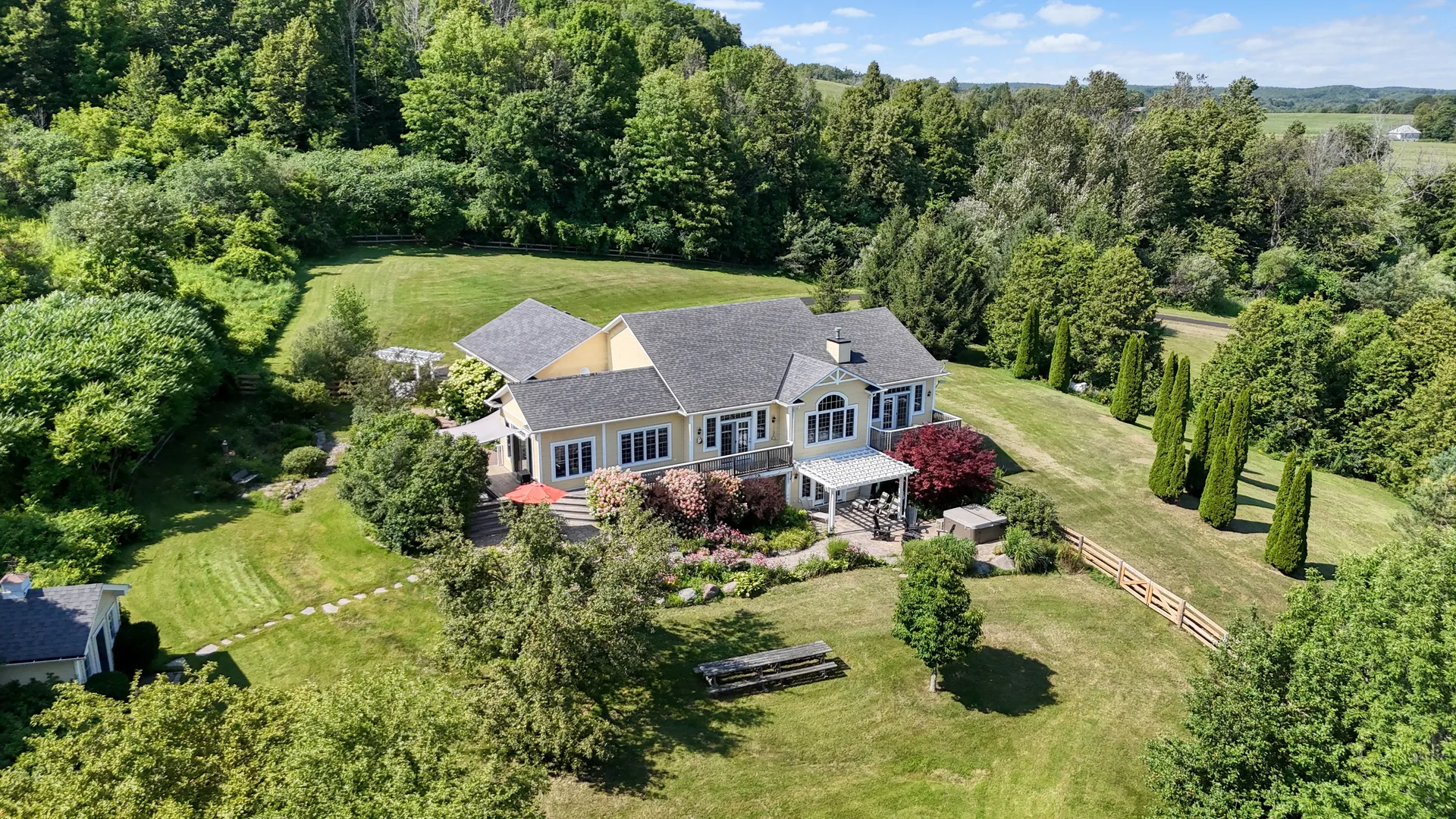 Aerial view of a suburban estate with yellow house, garden, and forest in Kingston Ontario