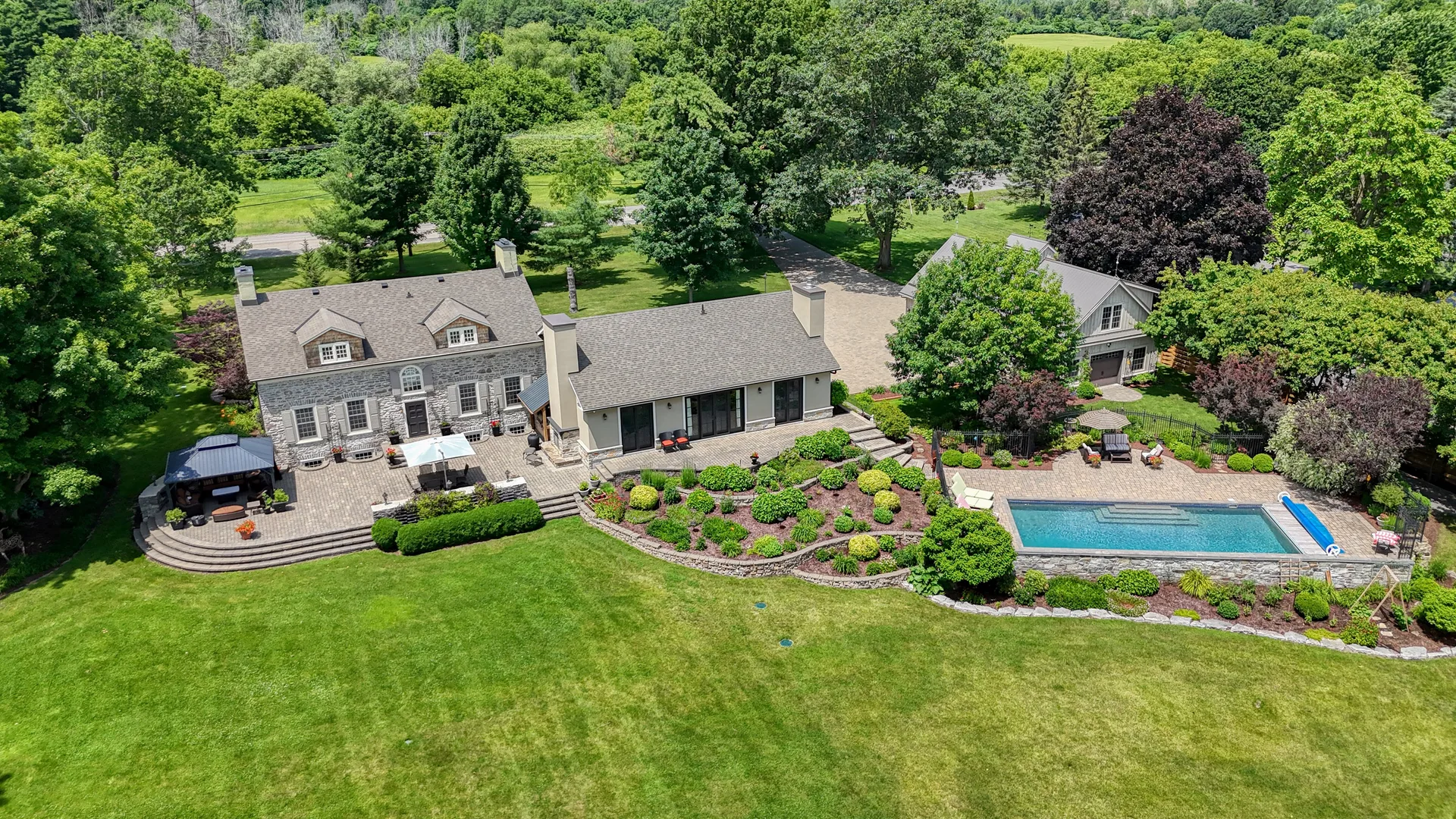 Aerial view of a luxury estate with stone house, patio, and swimming pool in Kingston Ontario