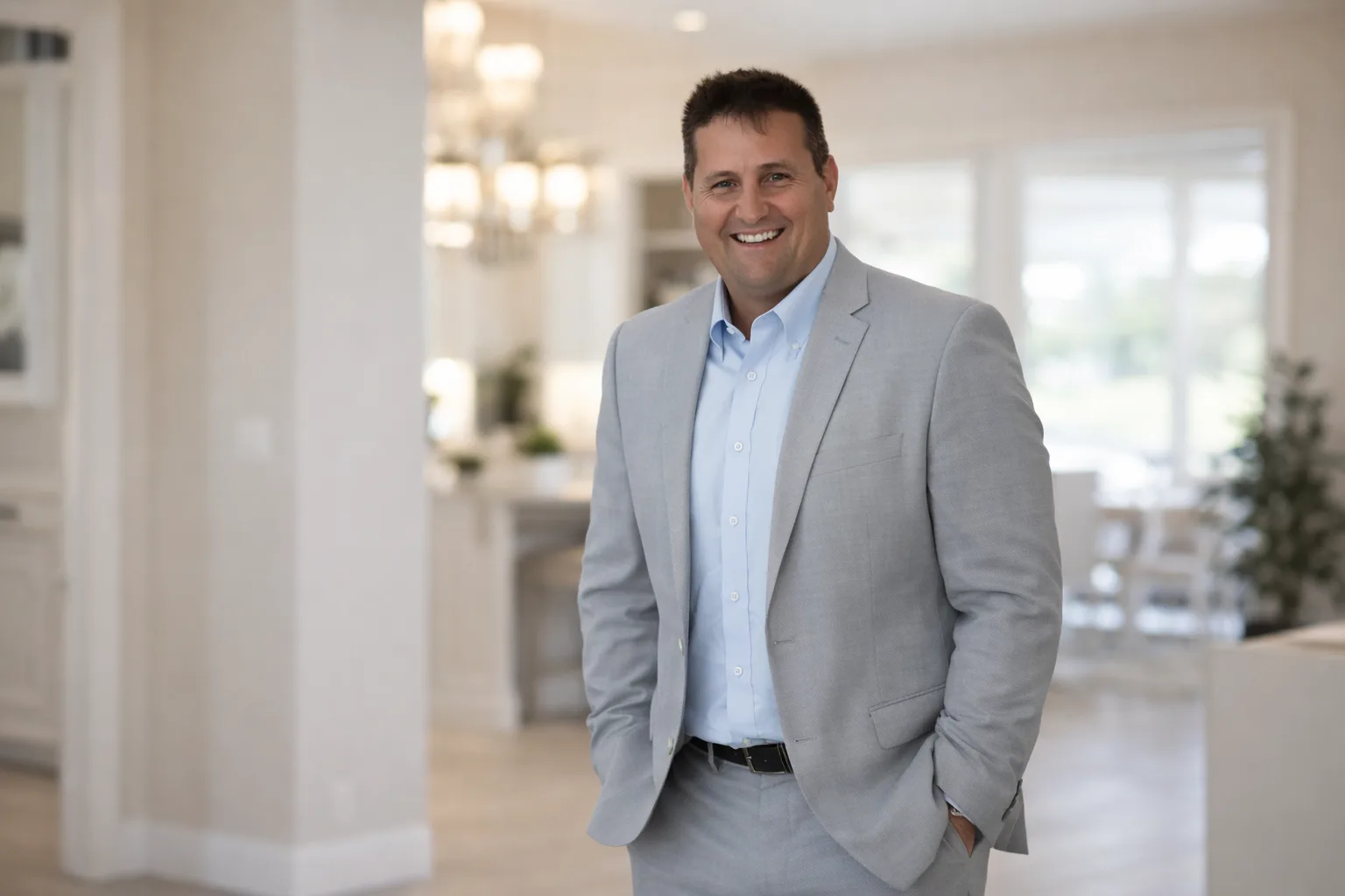 Professional portrait of Rob Dietrich in a light grey suit, standing in a bright home interior