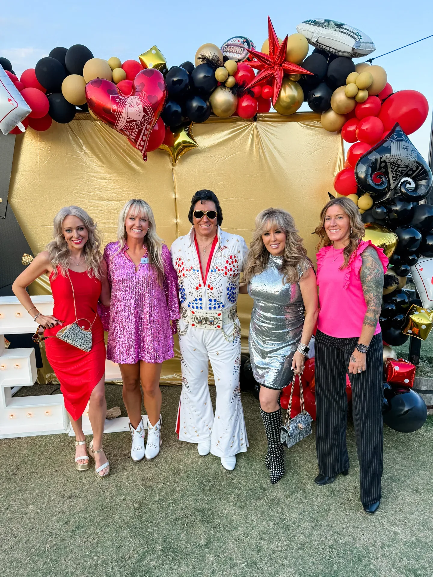 Lisa Copeland posing with an Elvis impersonator and a group in front of a casino-themed balloon arch