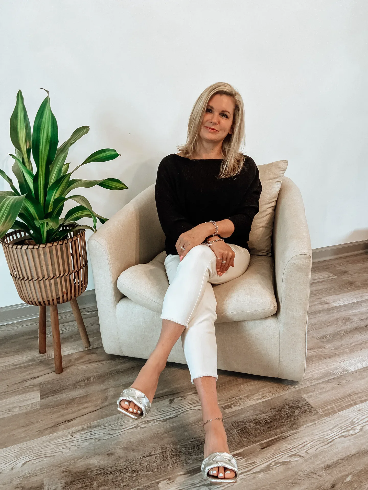 Michelle Lynn Jones, Realtor with eXp Realty, seated in an armchair wearing a black top and white pants