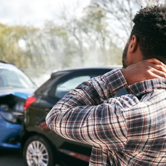 Man standing beside two damaged cars after a collision, holding his neck