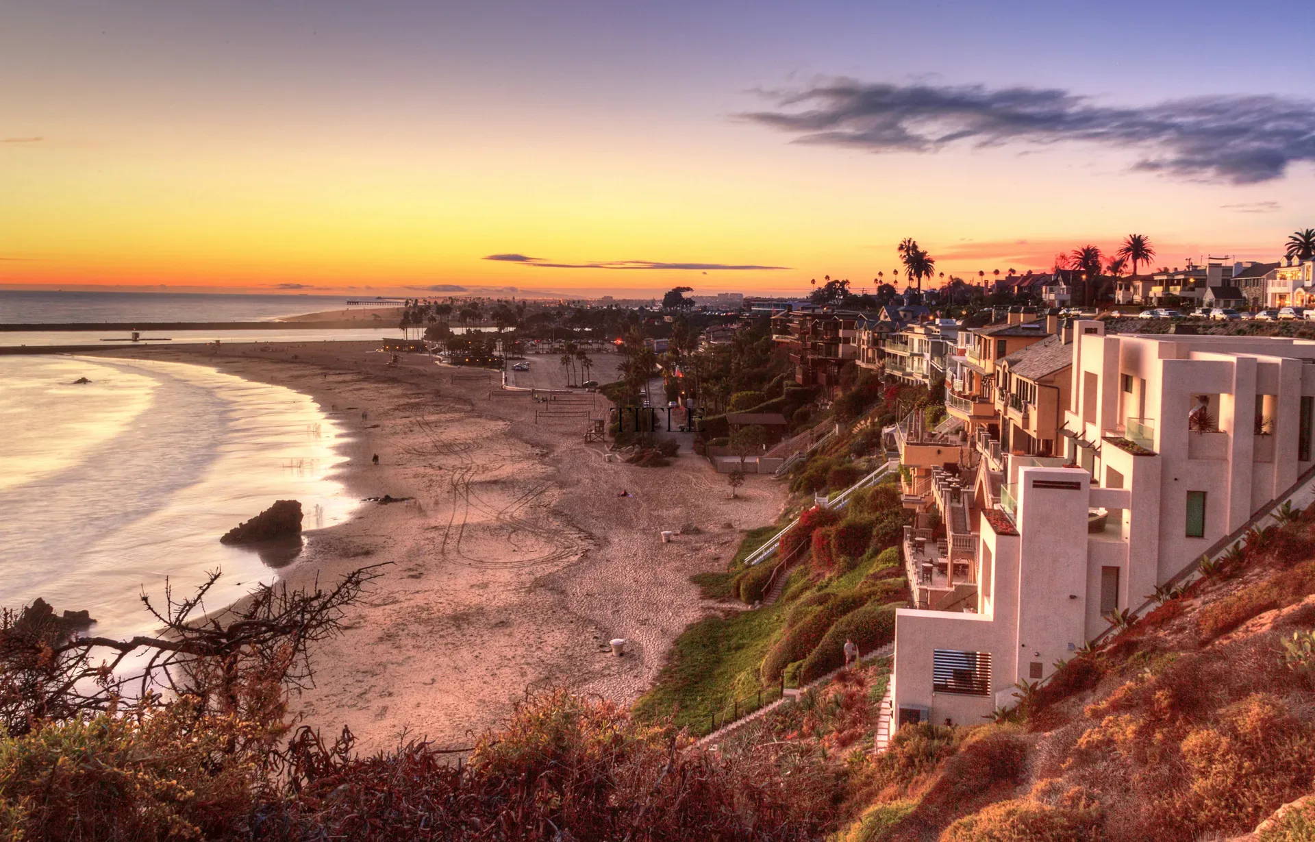 Wide-angle coastal beach neighborhood at sunset with luxury cliffside homes