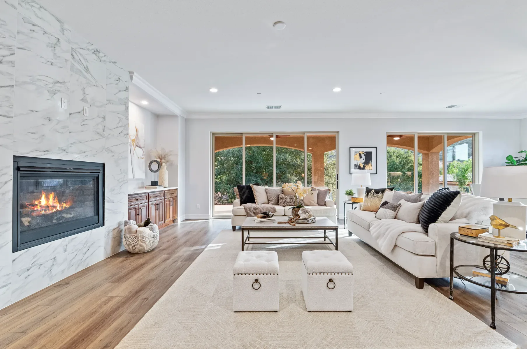 A bright, modern living room with a marble-accented fireplace and white furniture