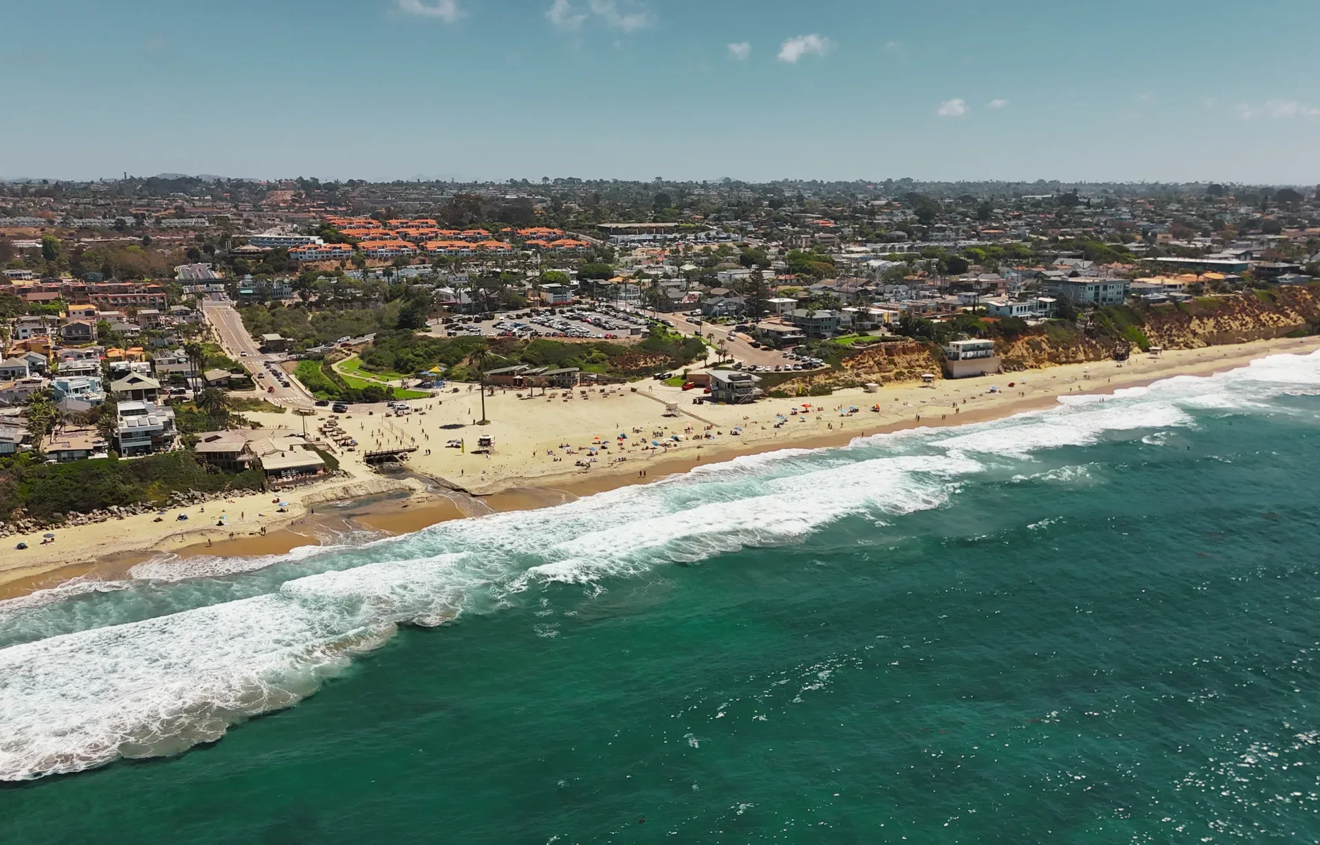 Aerial drone view of a coastal Encinitas neighborhood meeting the sandy beach and Pacific waves