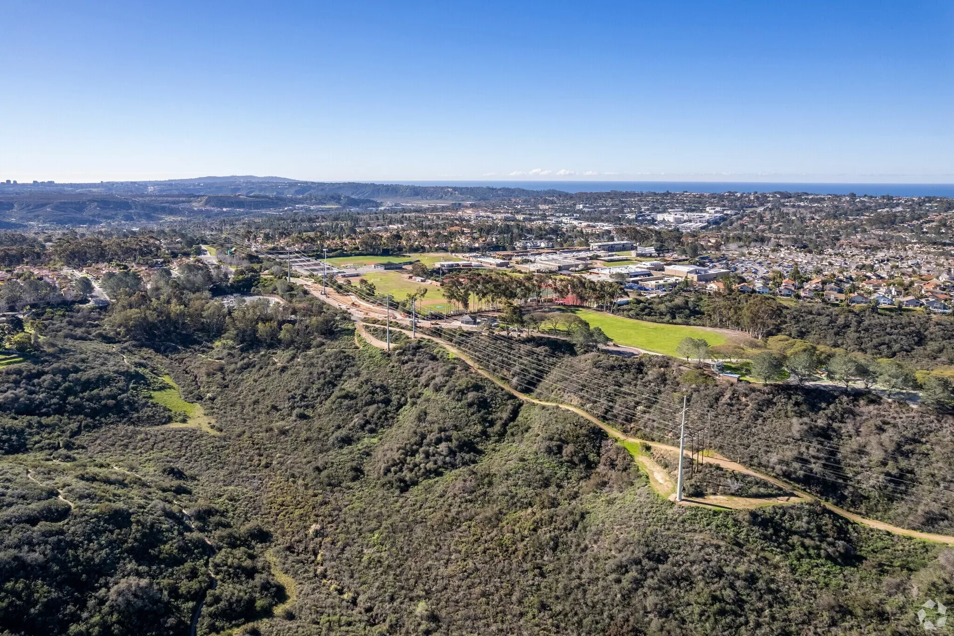 Aerial view of rolling green hills and residential areas with a distant ocean view near Carmel Valley