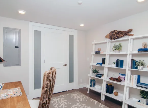 A bright coastal home office with white shelves, a wicker chair, and coastal decor