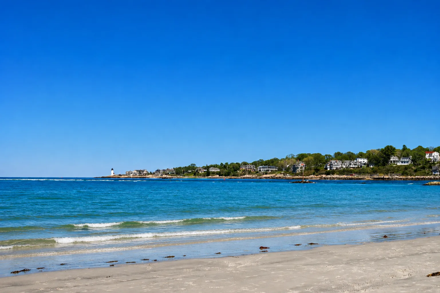 A sandy North Shore beach with turquoise water and a lighthouse in the distance under a clear blue sky