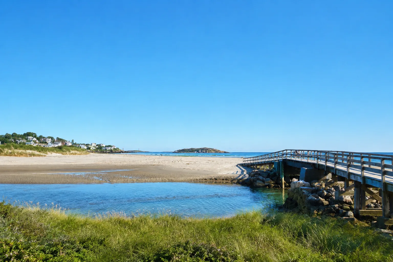 Sunny coastal landscape with a sandy beach, a wooden footbridge, and distant North Shore homes