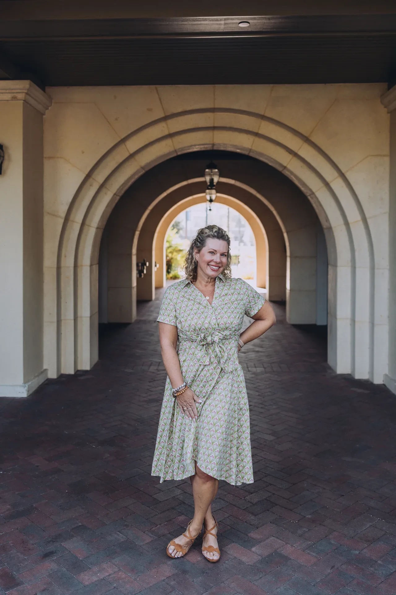 Mollie Younger smiling in a patterned dress beneath a light stone archway