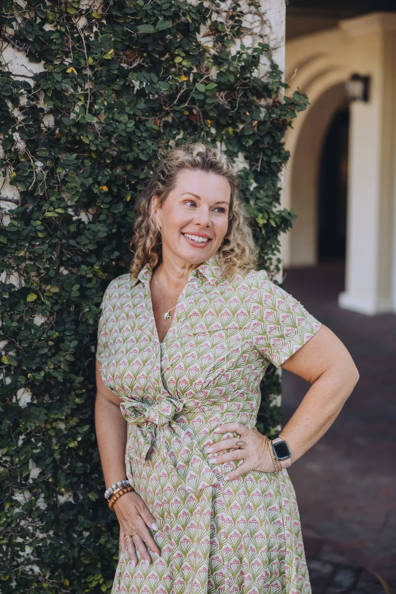 Mollie Younger, Ponte Vedra real estate advisor, smiling in a patterned green dress against a vine-covered wall