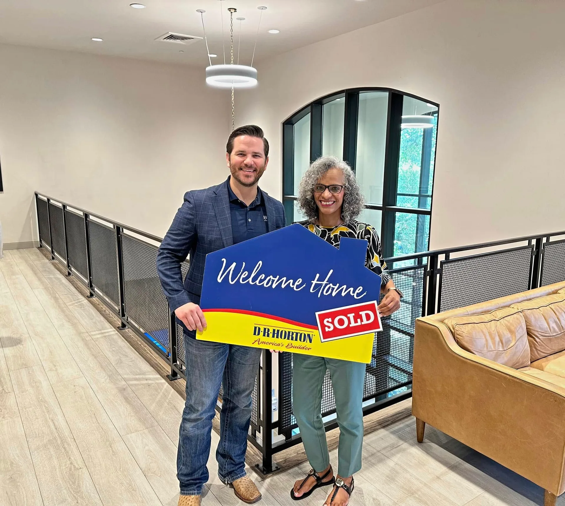 Tami Price with a client holding a house-shaped sold sign in a modern home interior