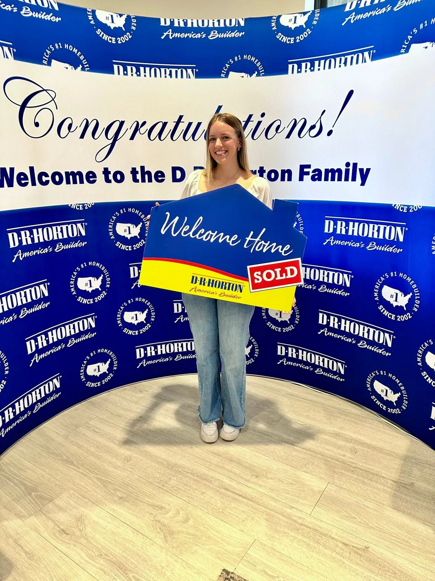 A client holding a Welcome Home Sold sign in front of a D.R. Horton backdrop