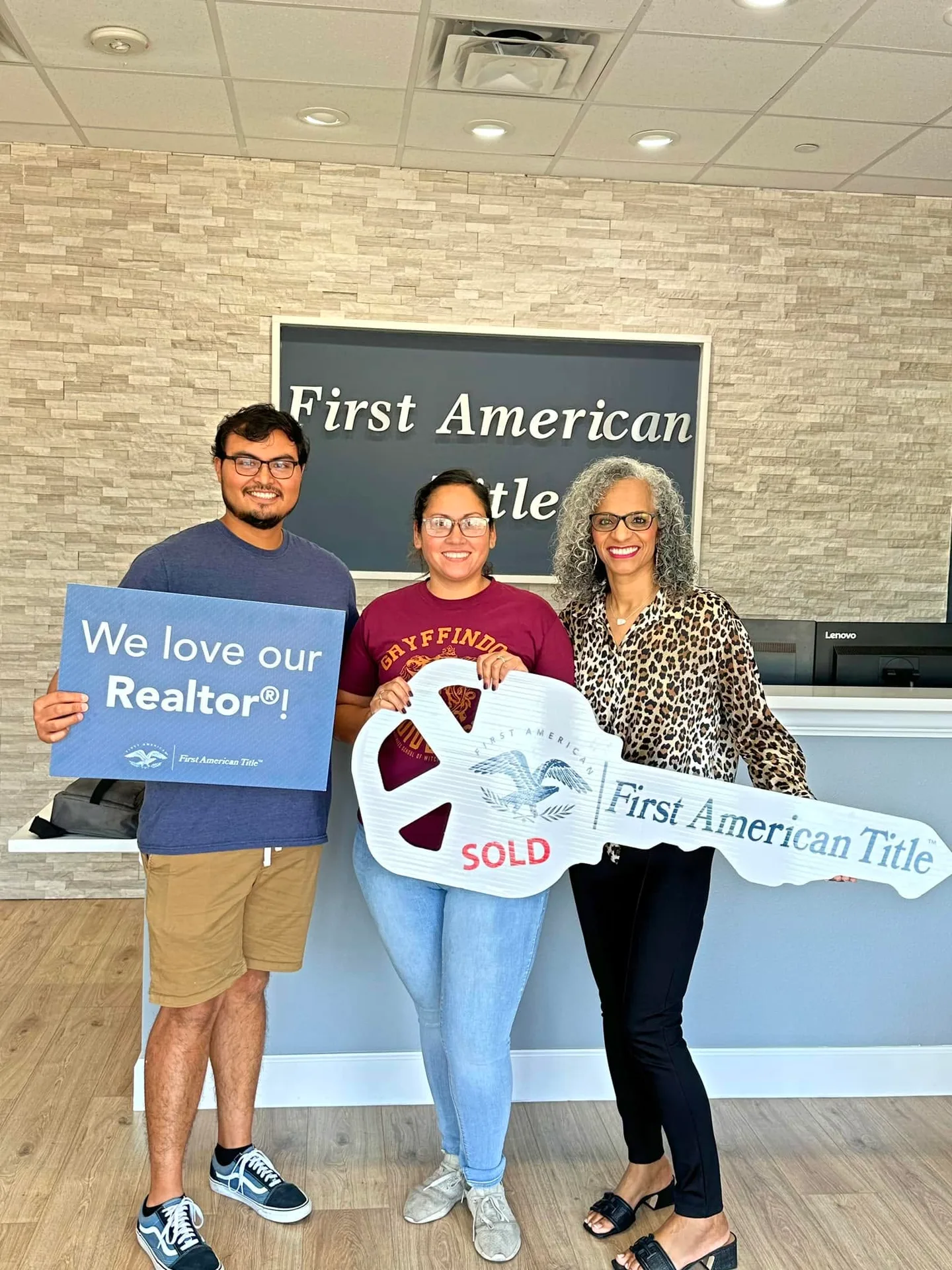 Tami Price with two clients holding a sold key and a sign in a title office
