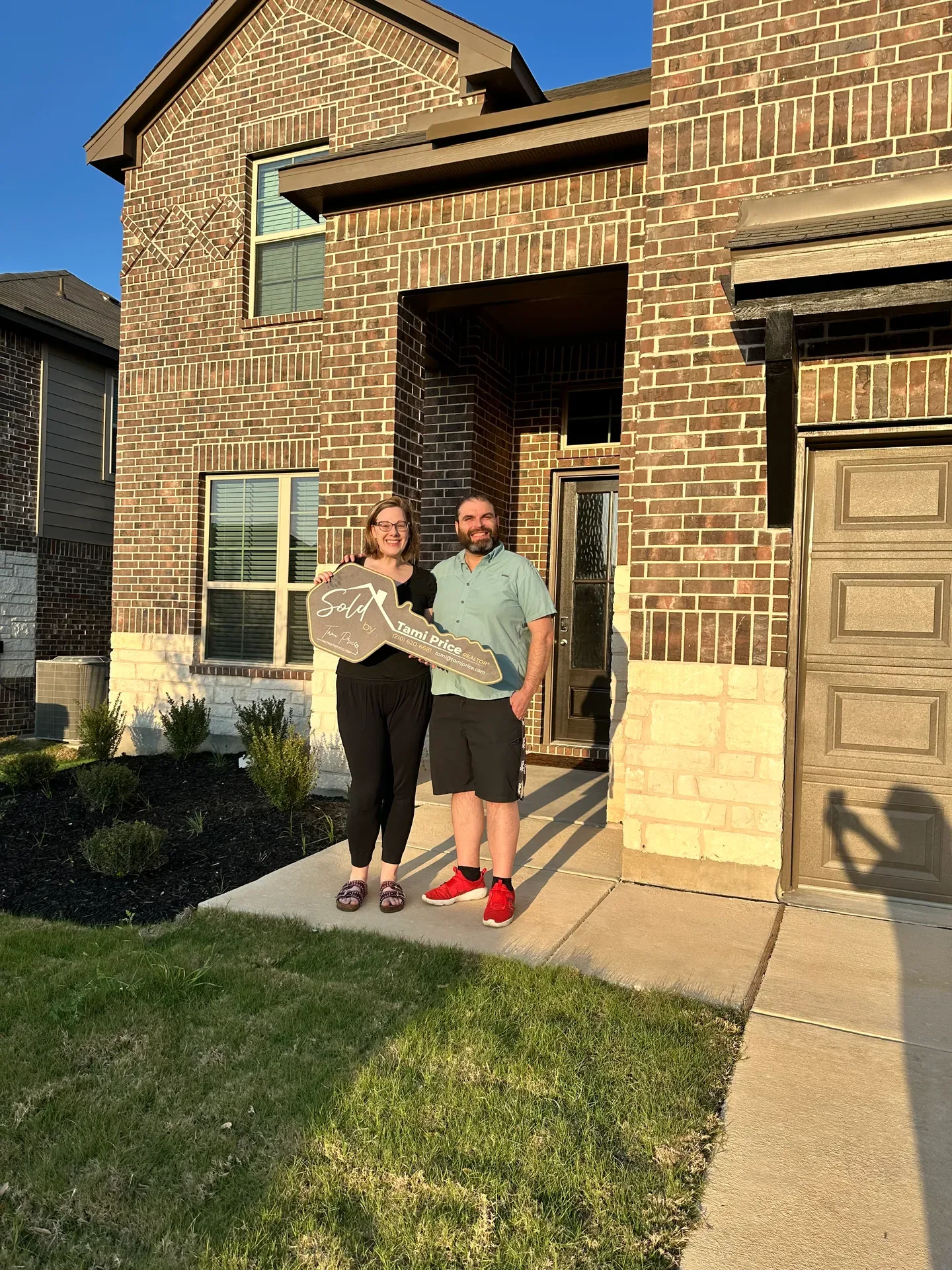 A couple celebrating on the front porch of their new home while holding a large Sold key on closing day