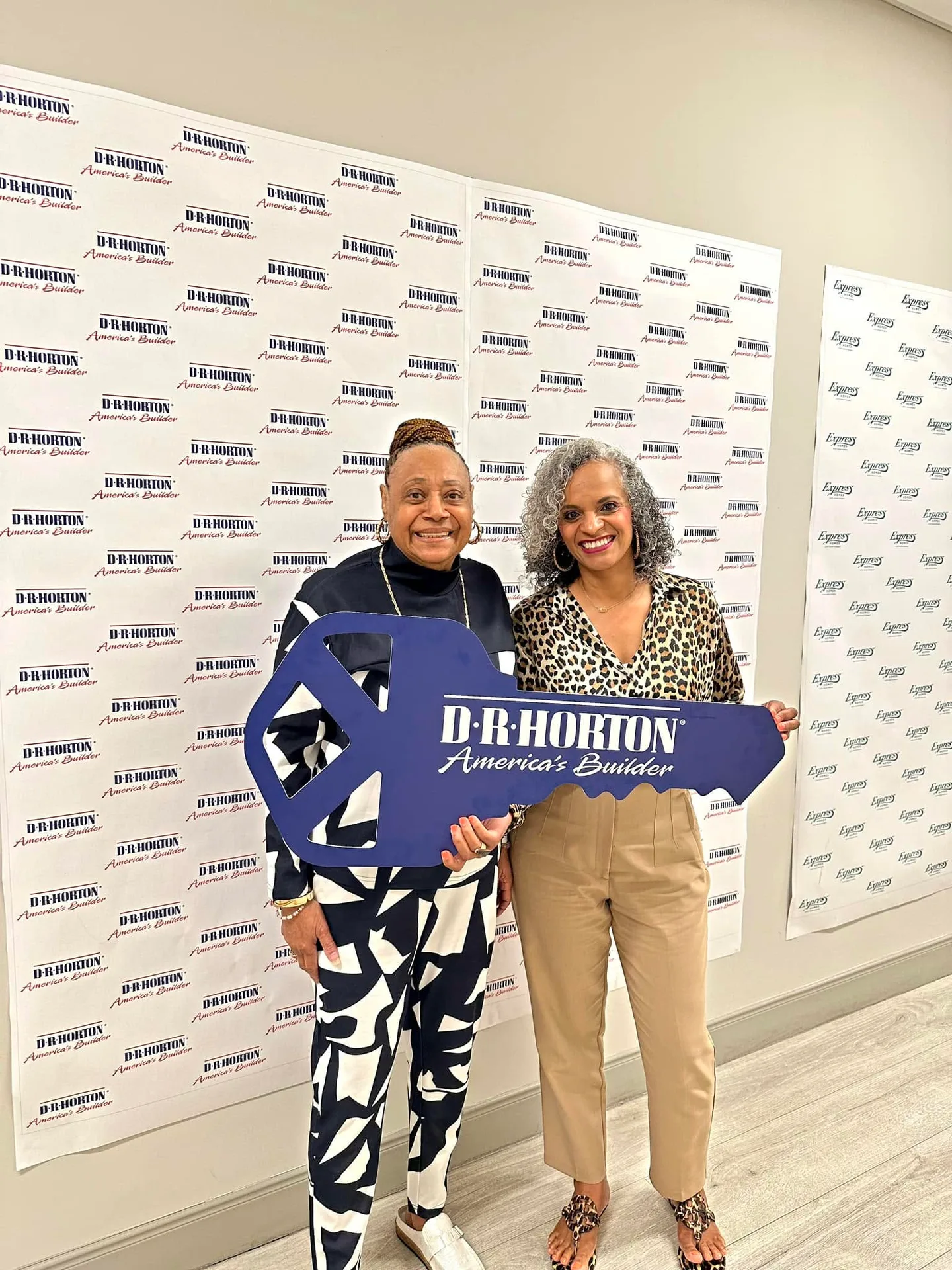 Two clients holding a large blue key against a D.R. Horton backdrop on closing day