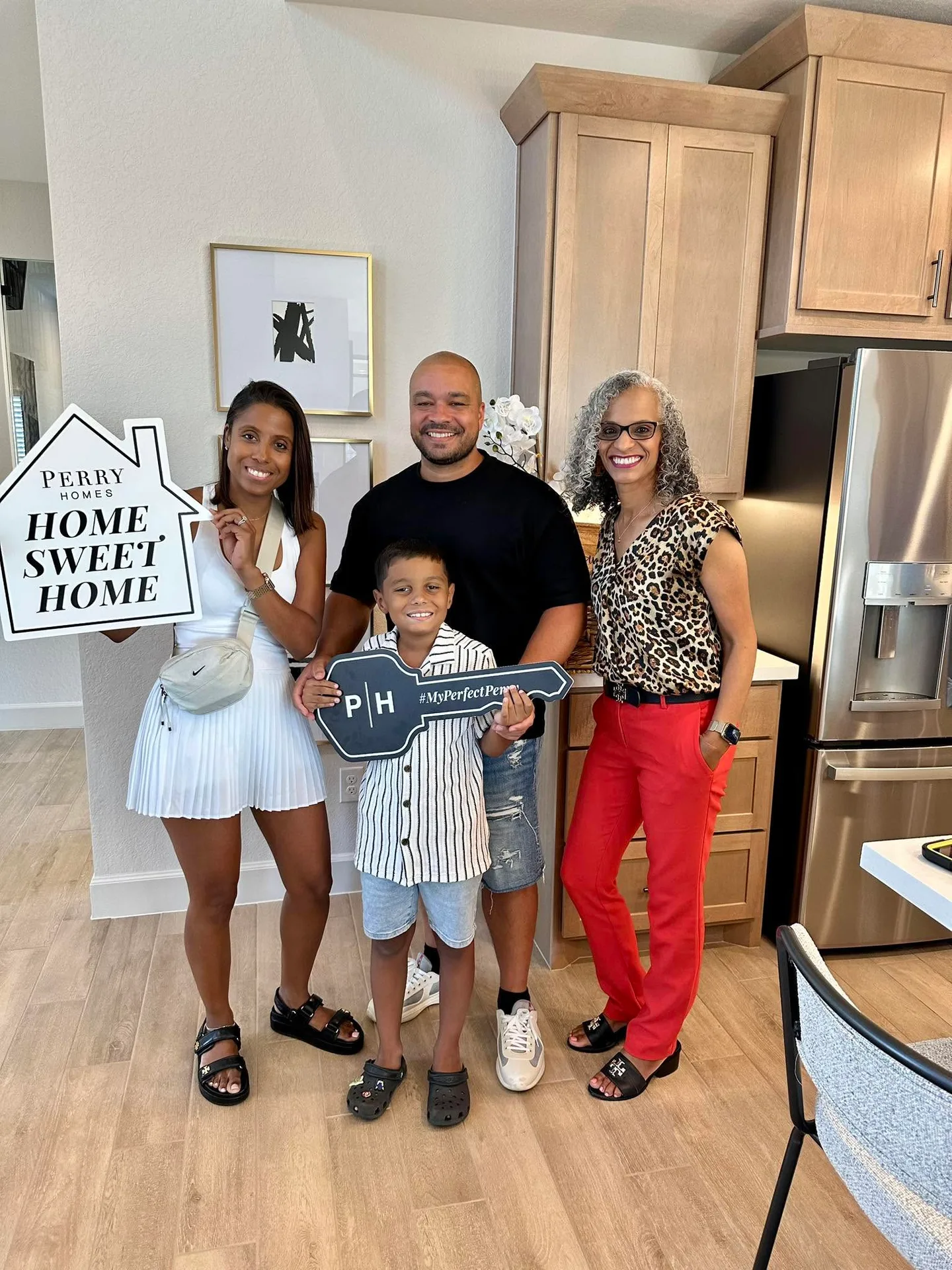 Tami Price with a family holding a house-shaped sign and a large key in a new home kitchen
