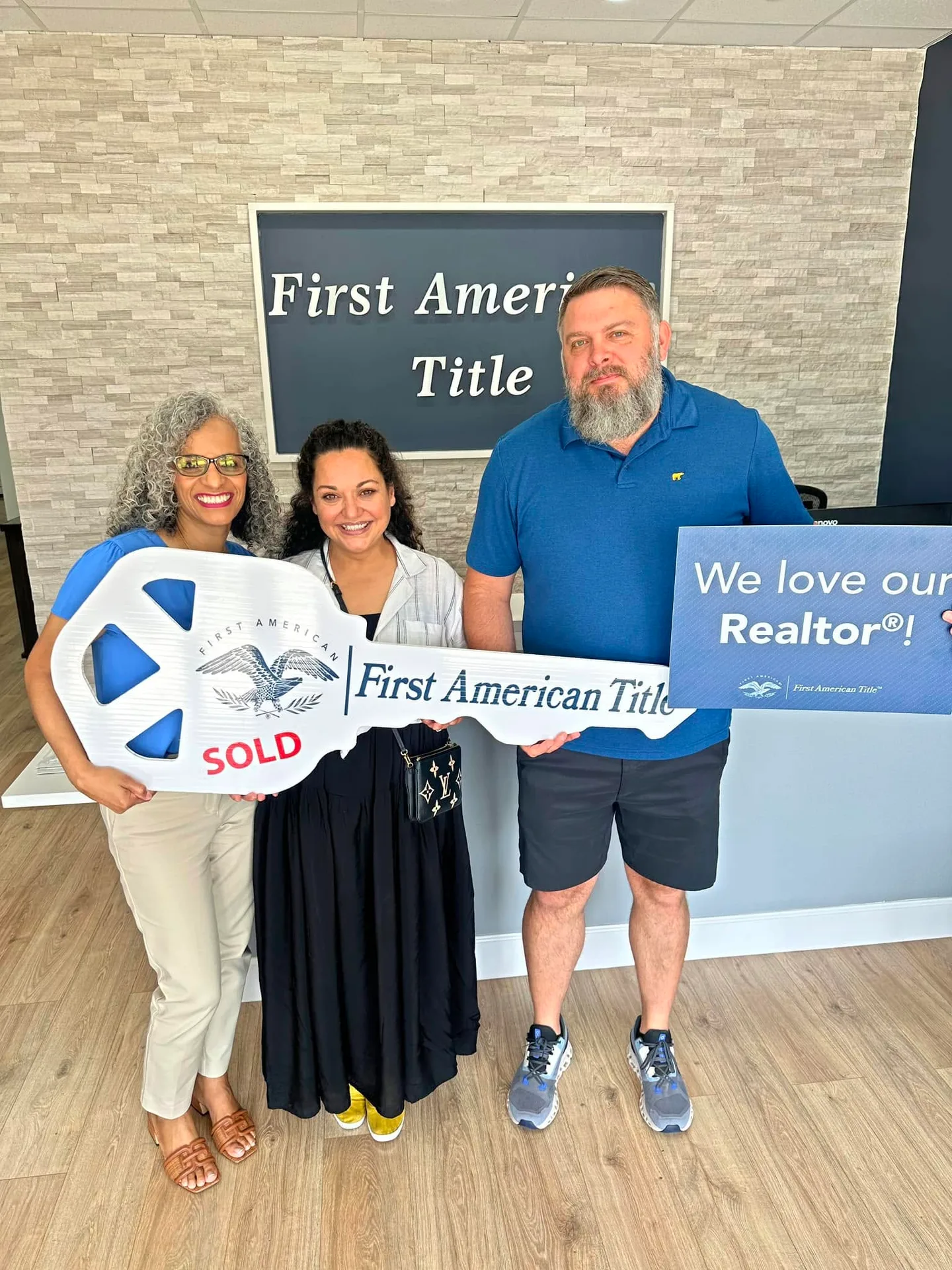 Tami Price with clients holding a large ceremonial key and a sign at a closing
