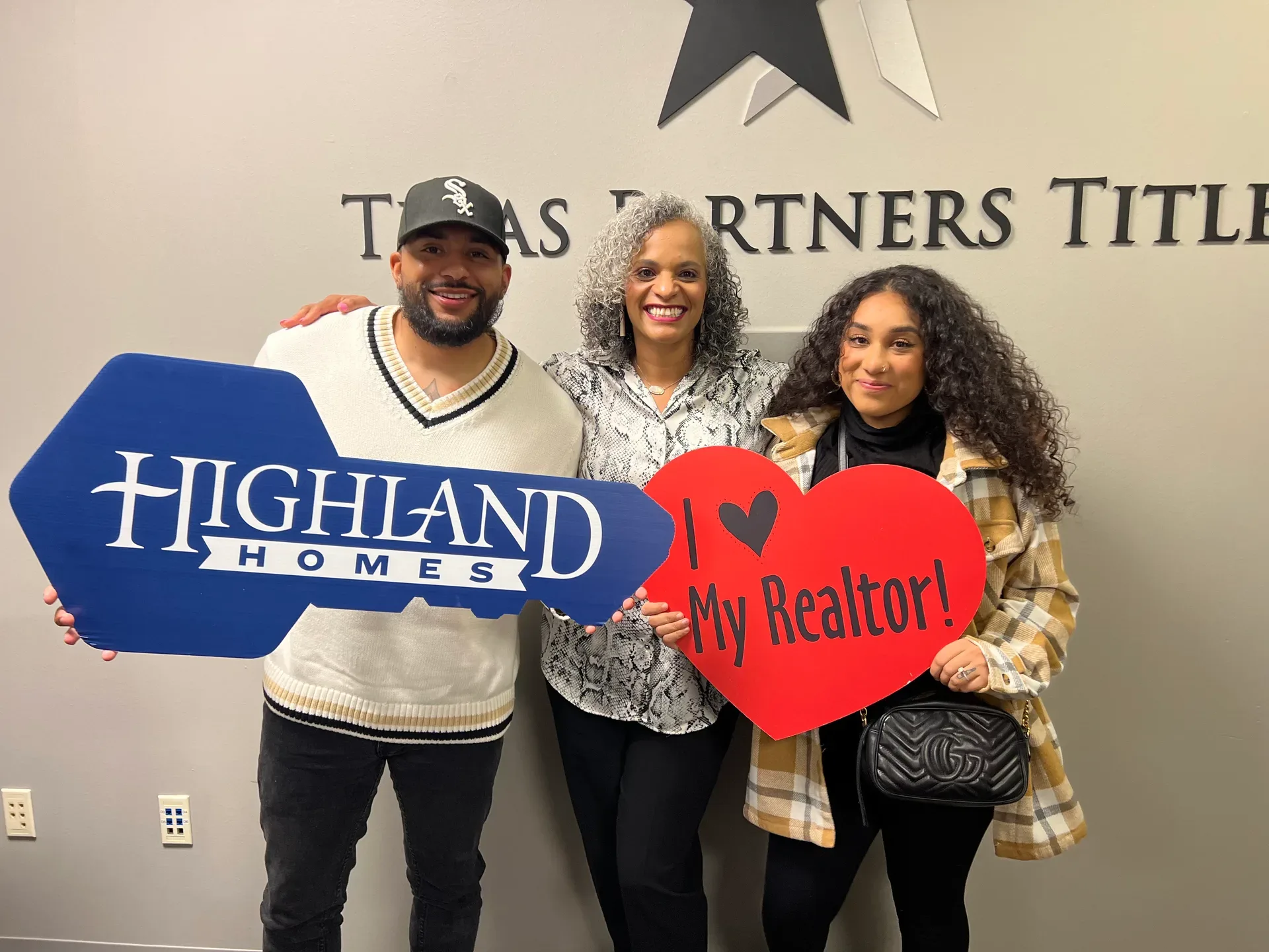 Tami Price with clients holding a large key cutout and an I Love My Realtor heart sign on closing day