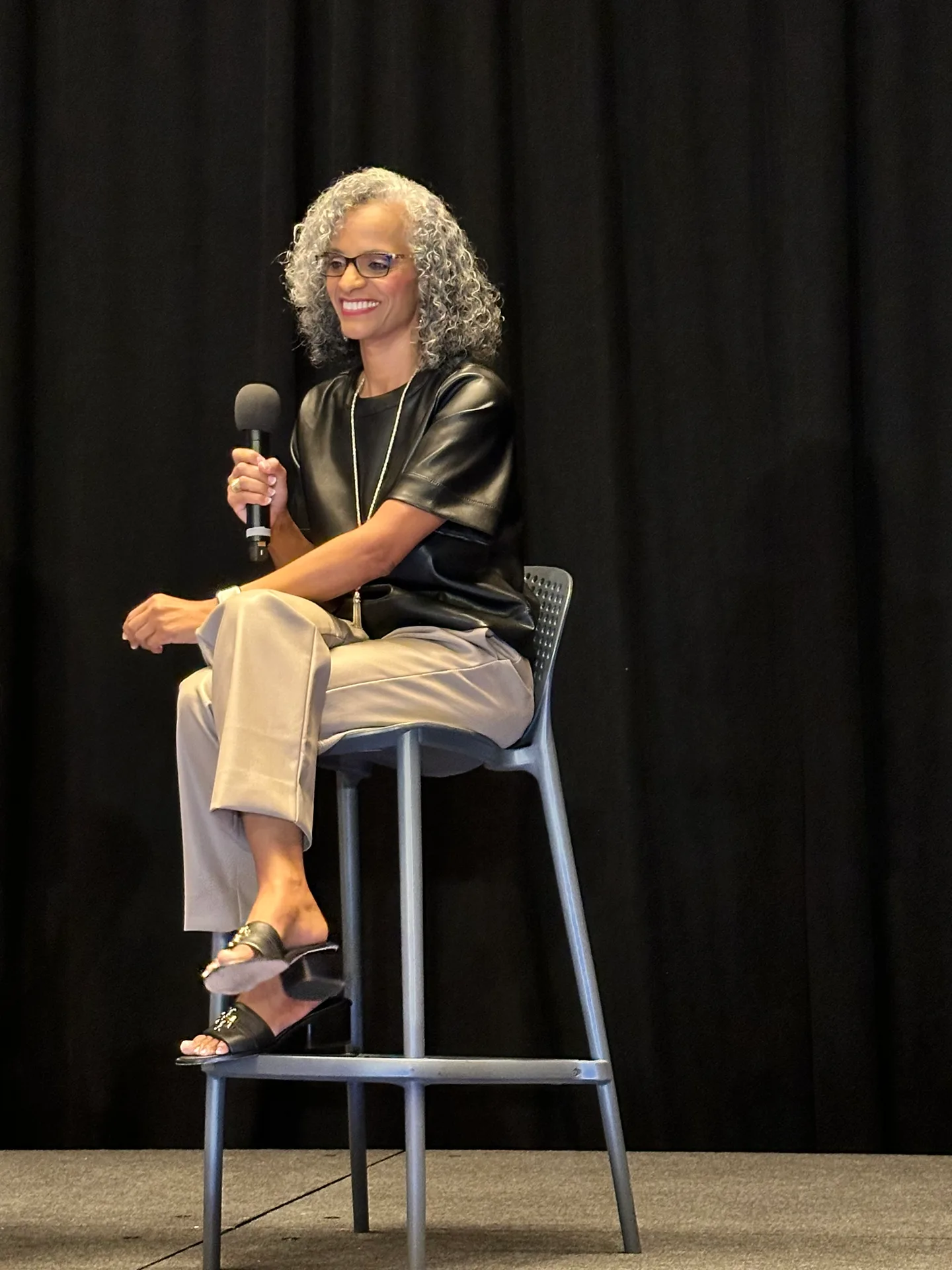 Tami Price speaking on stage with a microphone at a San Antonio industry event