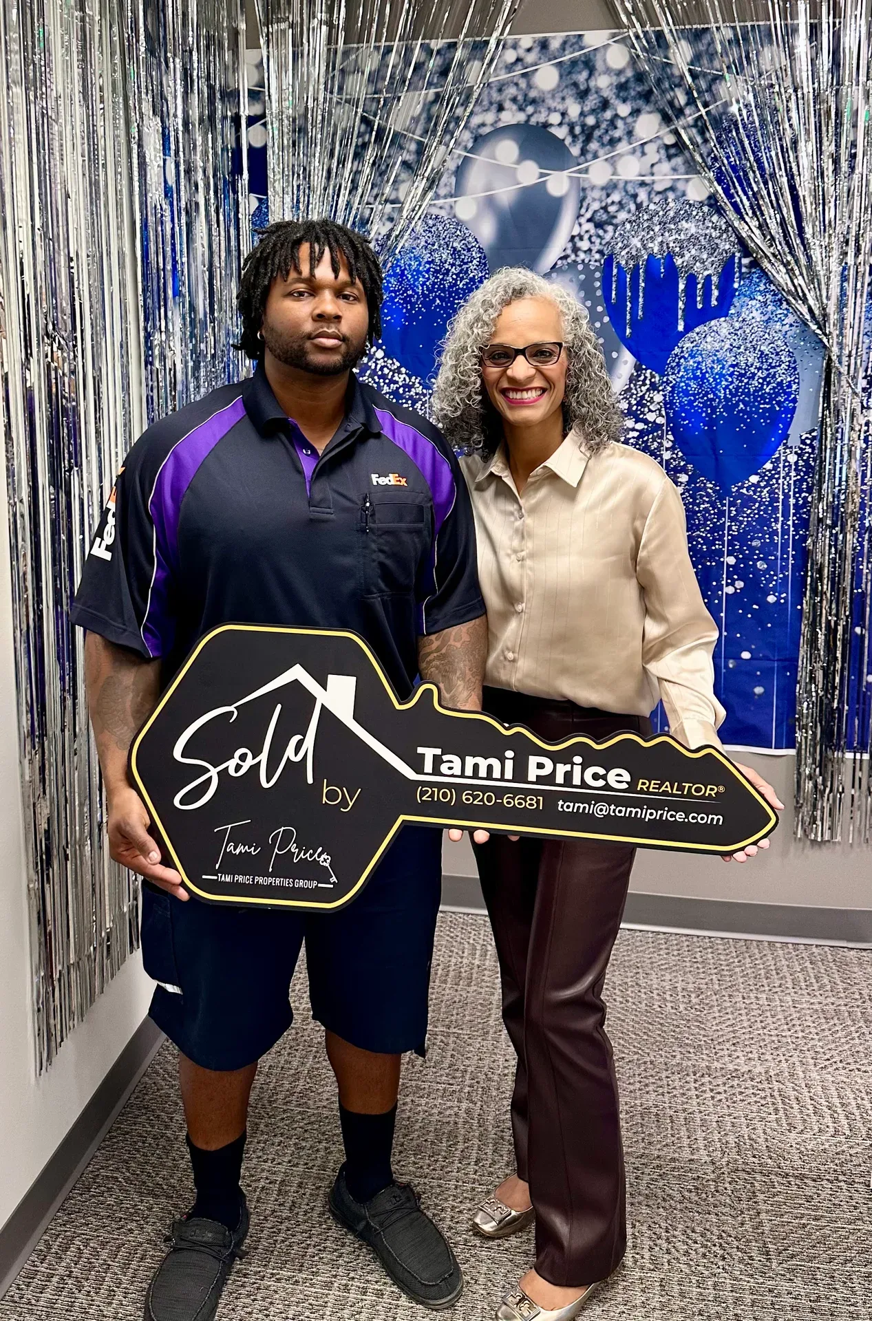 Tami Price with a client holding a large Sold key sign in front of a blue and silver balloon backdrop