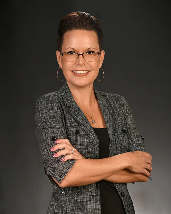 Mary Dover, Broker with Serenity Collective Real Estate, photographed with short dark hair, glasses, and a grey patterned blazer