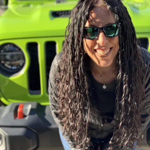 Belladonna Riso-Bayless smiling in sunglasses in front of her bright green lifted Jeep Gladiator