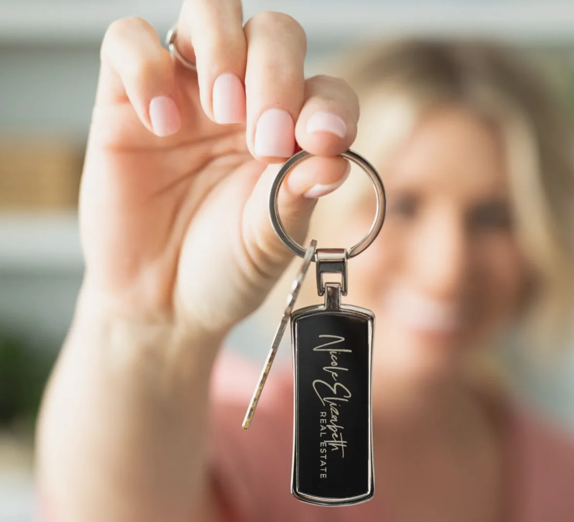 A hand holding a keychain with the Nicole Elizabeth Real Estate logo