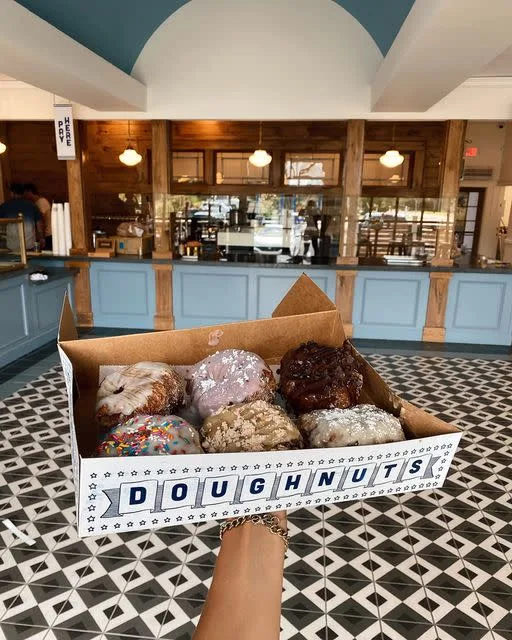 A hand holding a box of fresh doughnuts at Parlor Doughnuts