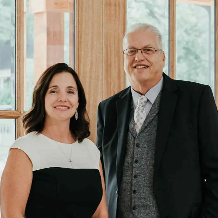 Craig Nash in a black suit with a gray vest and Anne Nash in a black and white dress, standing together indoors