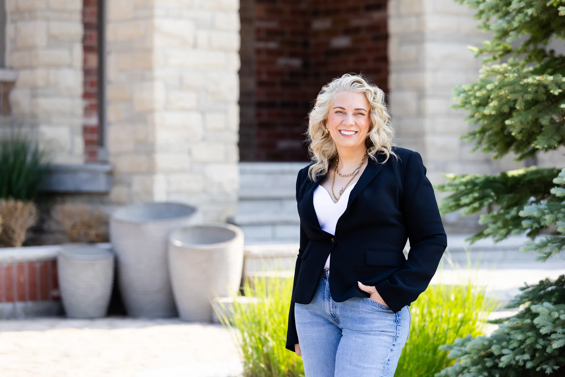 Professional outdoor portrait of Kelly MacDonald-Wilson, REALTOR and Advisor, standing in front of a stone home in Halton Hills