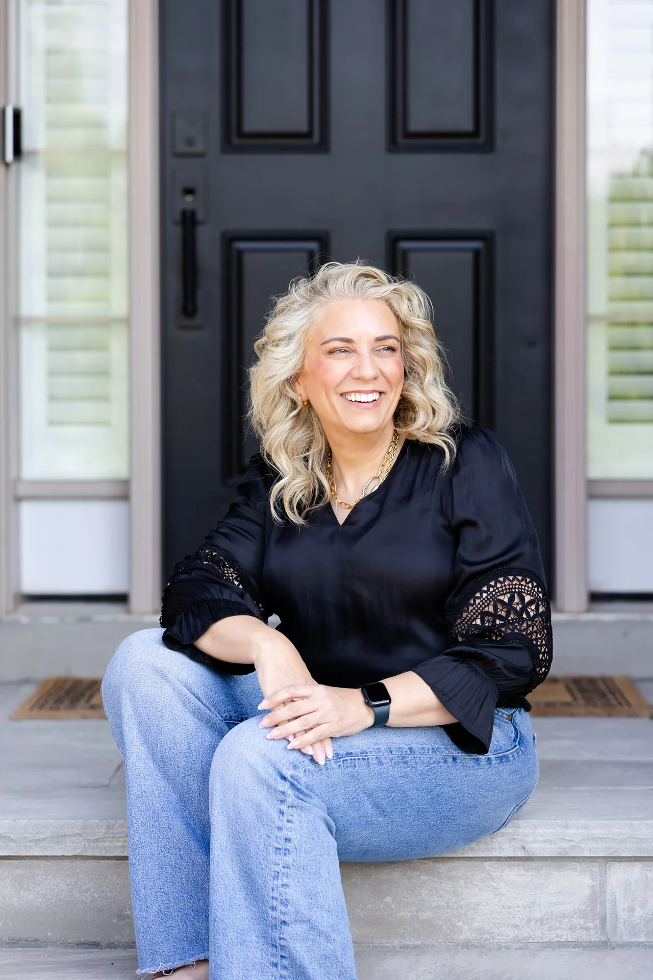 Kelly MacDonald-Wilson sitting on the front porch steps of a Halton Hills home, smiling in a black blouse and jeans