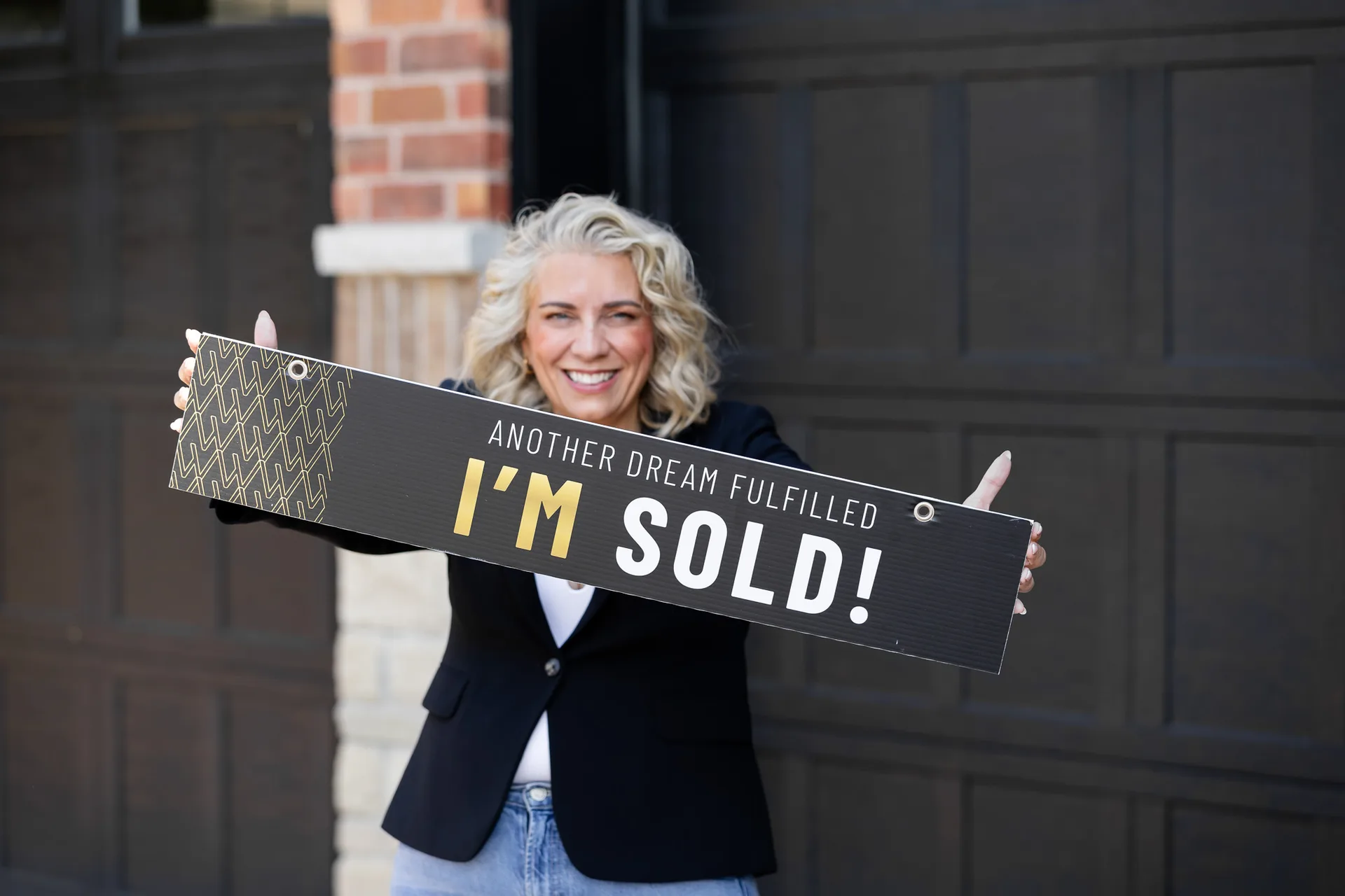 Kelly MacDonald-Wilson celebrating a client's sale, smiling while holding an I'm Sold sign outside a Halton Hills home