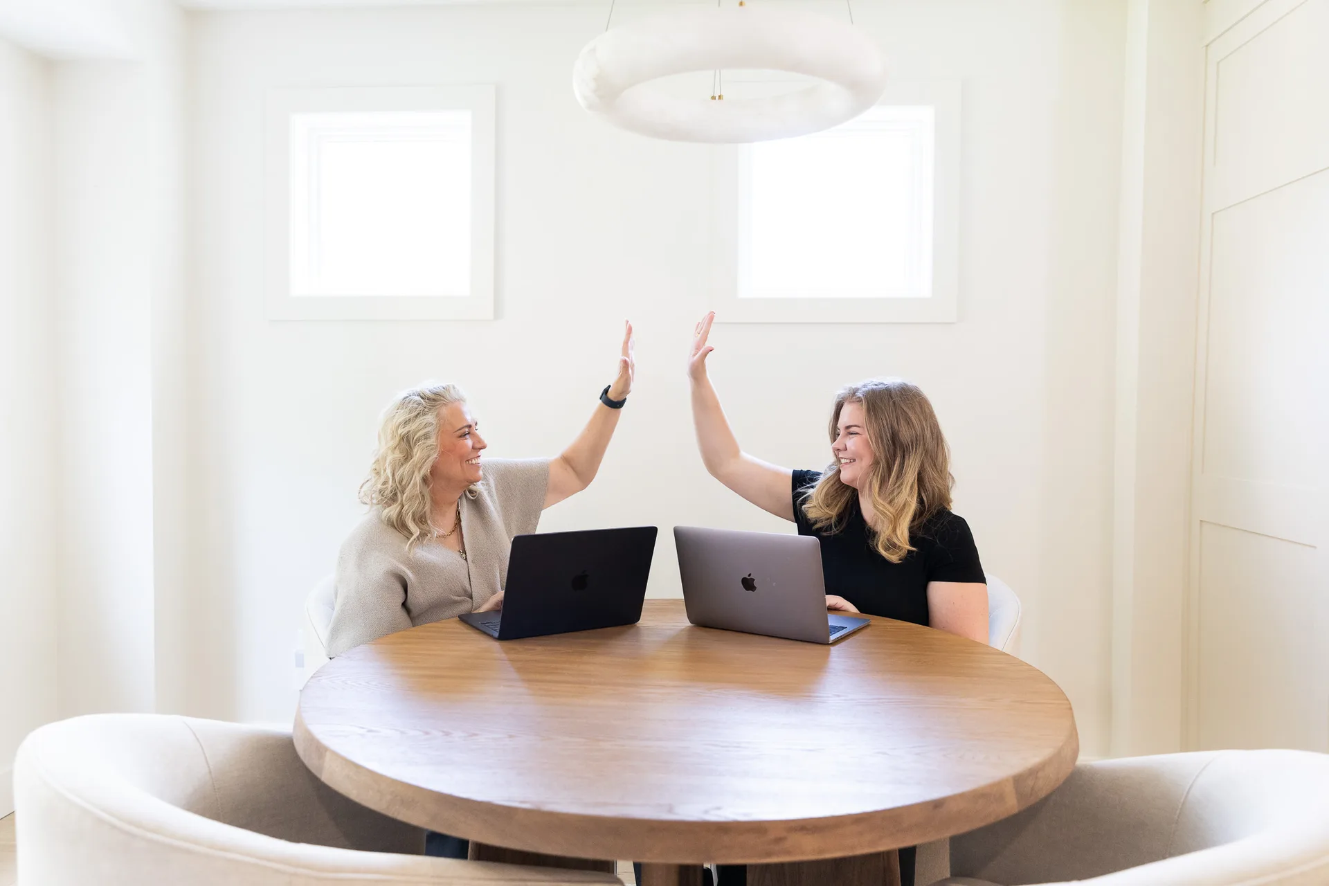 Kelly MacDonald-Wilson and a colleague giving each other a high-five across a shared table while planning a client's move