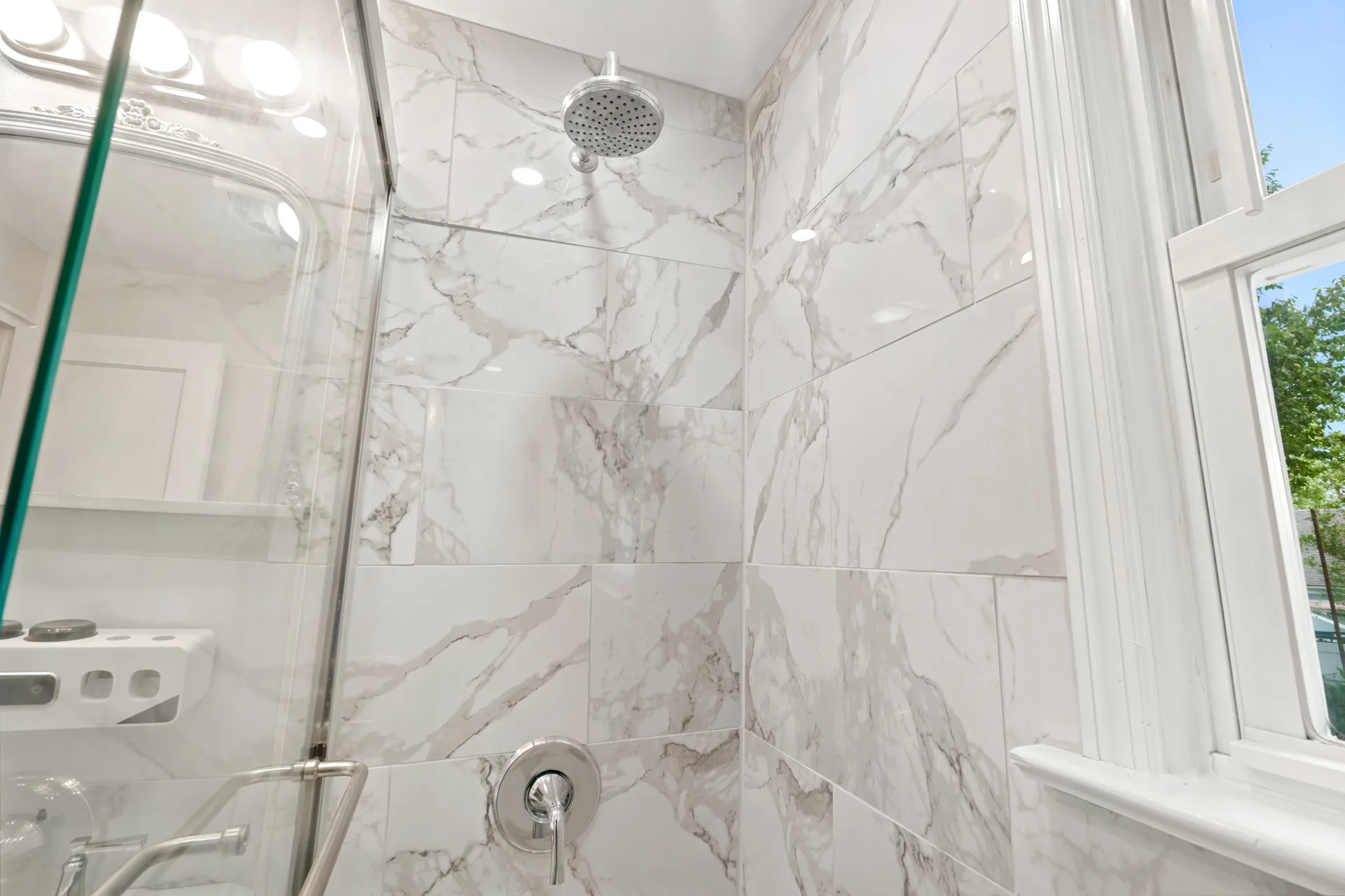 Modern shower enclosure with large white marble-look tiles and chrome rain shower head