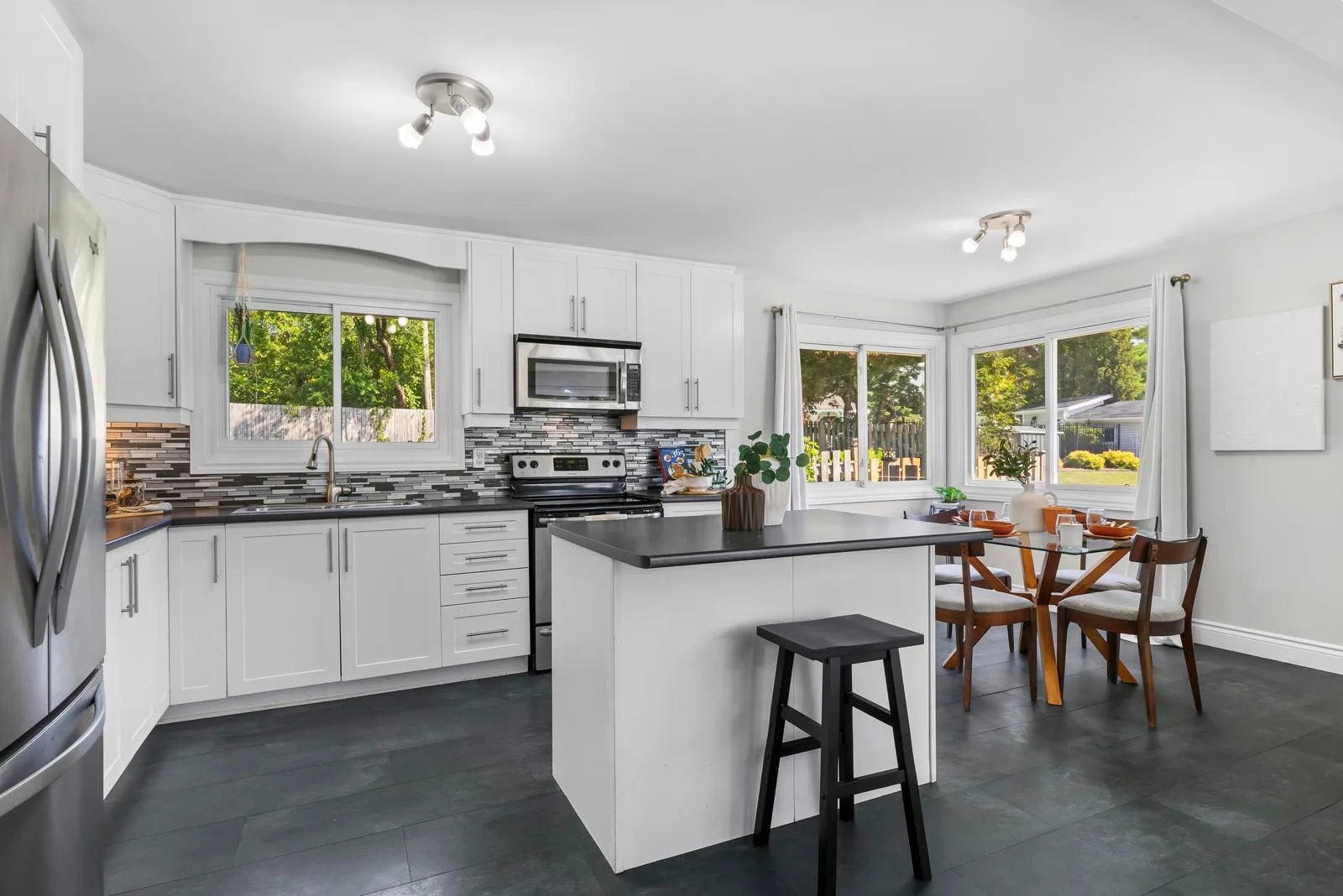 Wide-angle view of eat-in kitchen with island, white cabinetry, and dark tile flooring