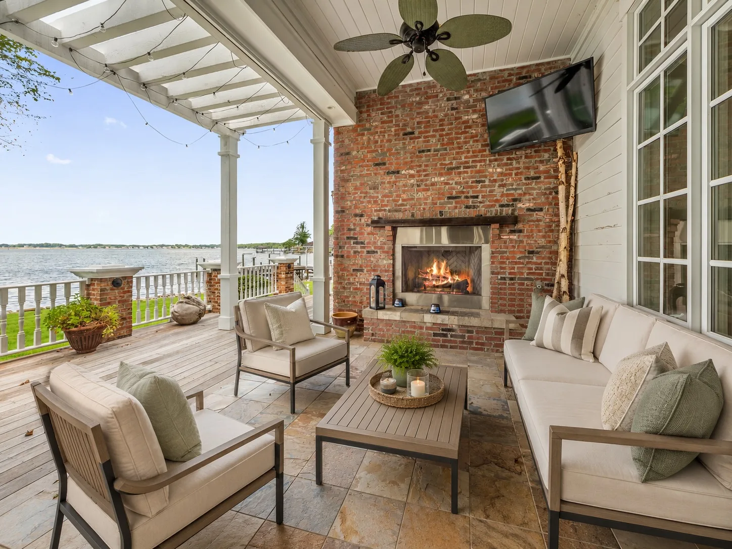 Covered outdoor patio with brick fireplace, lakefront views, and pergola ceiling