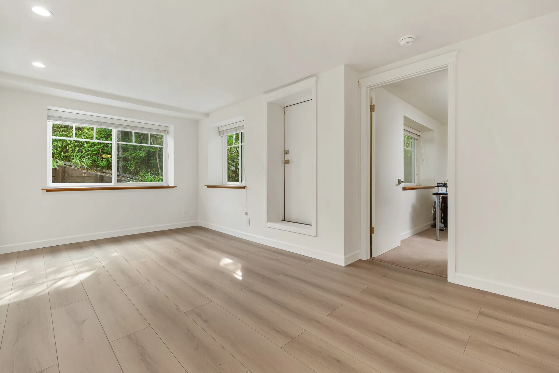 Bright flex room with white walls and dual windows looking out to greenery
