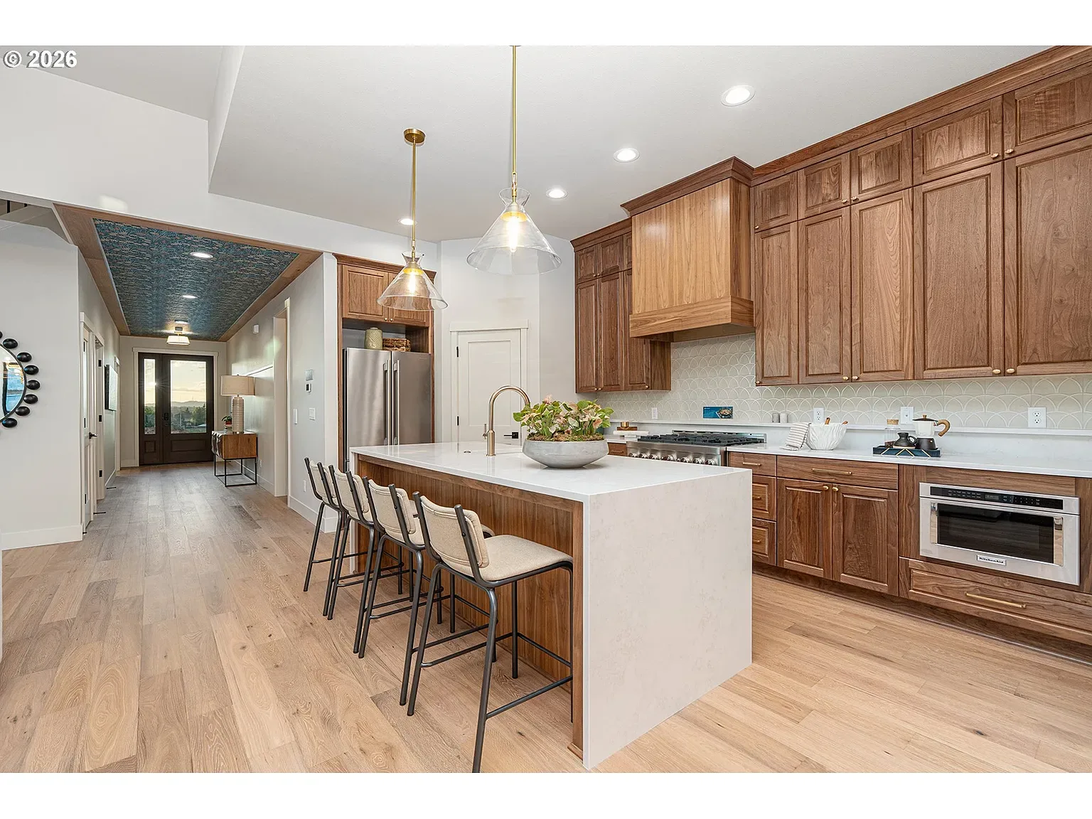 Island & hall: Textured ceiling, warm wood, and a stone waterfall island
