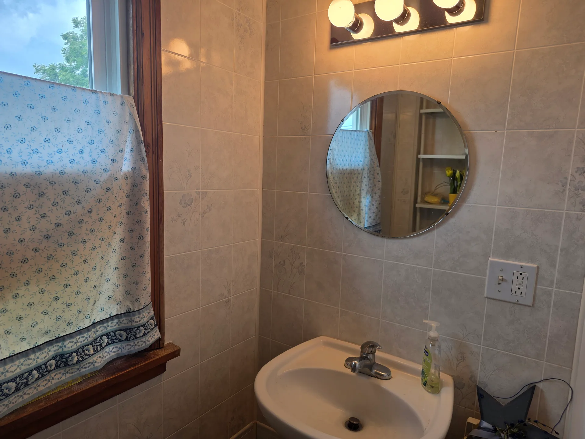 Bathroom vanity area with tiled walls, pedestal sink, and circular mirror